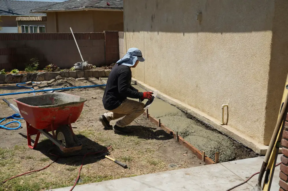 A masonry contractor setting up a concrete barrier around the structure of the external garage